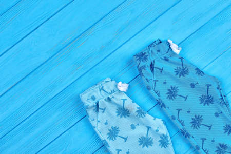 Childs clothing summer background. Blue patterned baby summer trousers folded on blue wooden background, copy space.の写真素材