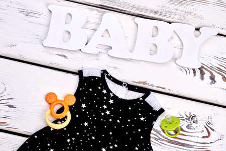 Infant girl black patterned dress. Baby-girl sleeveless cotton sundress, teether, pacifier, white wooden background.の写真素材