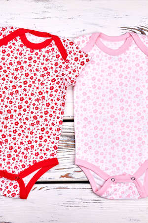 Set of beautiful bodysuit for newborn girls. New soft summer rompers for infant girls on old wooden background, top view.の写真素材