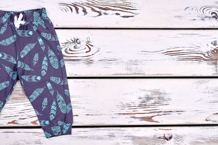 Baby boy dark printed harems. Toddler boy cute patterned tousers, old wooden background, copy space.