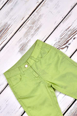 Kids green trousers, top view. Brand high quality trousers for little girl on old wooden background. Kids fashion apparel.の写真素材
