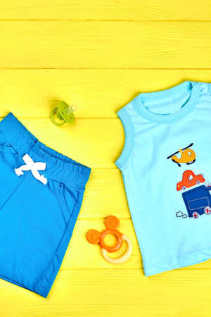 Infant boy summer clothes background. Baby boy cute summer garment, accessories on yellow wooden...