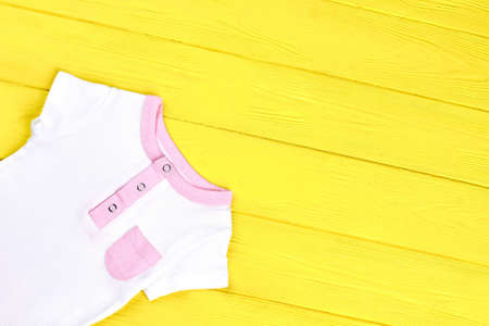 Infant girl cute textured t-shirt. Baby-girl white romper with pink pocket on colored wooden background, copy space.の写真素材