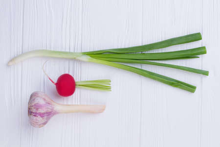 Fresh spring vegetables on white wood. Young garlic, onion and radish on wooden table. Cooking spring healthy salad.の写真素材