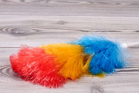 Fluffy duster brush on wooden background. Close up soft colorful duster with plastic handle on wooden background. House cleaning supply.の写真素材