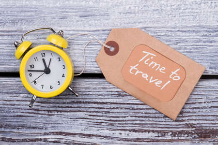 Yellow clock and label. Time to travel. Wooden desk surface background, flat lay.の写真素材
