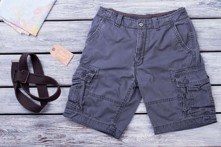 Travel clothes and equipment. Black shorts, map and strap. Wooden desk surface background.の写真素材
