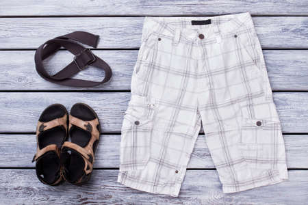 Male summer apparel, flat lay. White checkered male shorts, sandals and strap.の写真素材