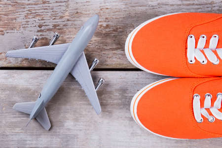 Red shoes and toy airplane. Flat lay, top view. Wooden desk surface background.