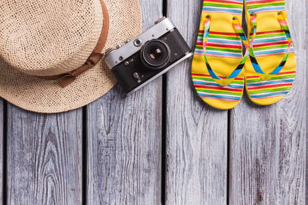 Straw hat, vintage photo camera and flip-flops. Top view, flat lay, summer, beach and travel concept. Wooden desk surface.の写真素材
