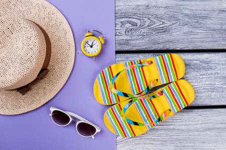 Beach items for resort flat lay. Top view, straw hat, alarm clock, sunglasses and flip-flops.