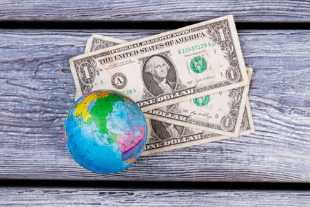 Globe and money flat lay. American dollars and globe on wooden desk surface.の写真素材