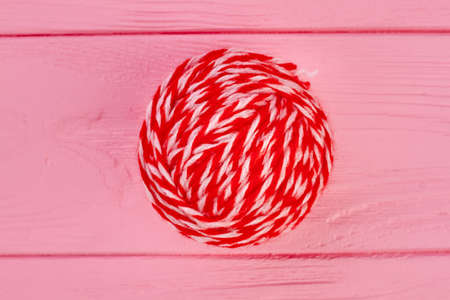 Close up red ball of woollen threads. Red ball of yarn for knitting on pink wooden background.