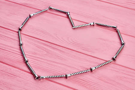 Shape of heart from hardware products. Metal screws forming heart shape on pink wooden background. Metal love concept.の写真素材