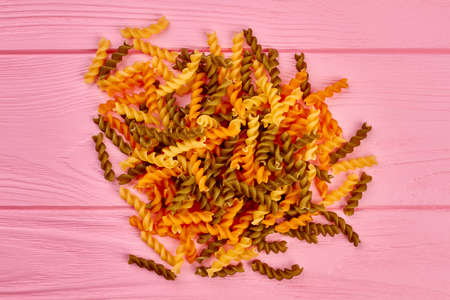 Heap of colorful spiral macaroni, top view. Group of colorful fusilli pasta on pink wooden backgorund. Traditional itatlian food.の写真素材