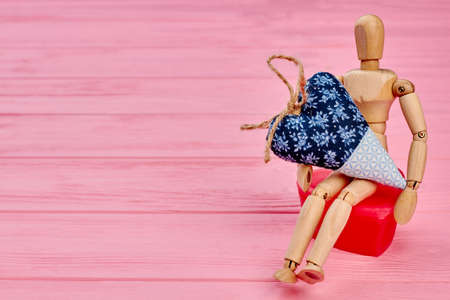 Human wooden dummy with heart, copy space. Human wooden mannequin sitting and holding big heart. Valentines Day concept.の写真素材
