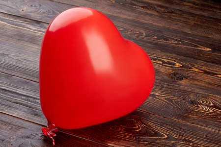 Heart shaped balloon on wooden background. Red balloon in a shape of heart filled with oxygen on brown wooden background.の写真素材