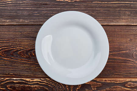 White empty plate, top view. Porcelain plate on brown wooden background.の写真素材