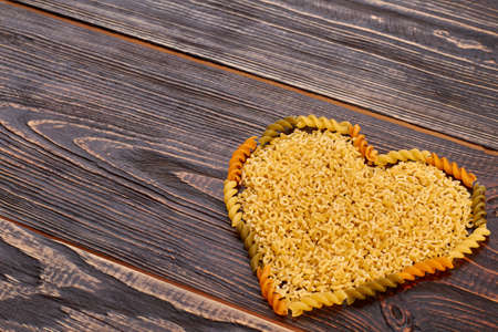 Valentines Day background with pasta in heart shape. Uncooked macaroni forming heart shape, copy space. Valentines holiday greeting card.の写真素材