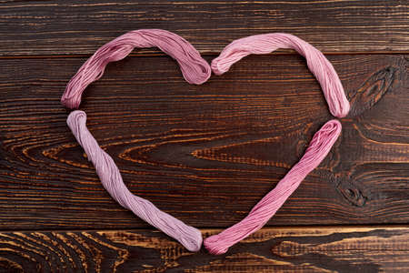 Heart shape from colorful threads. Bundles of pink threads forming heart on brown wooden background.