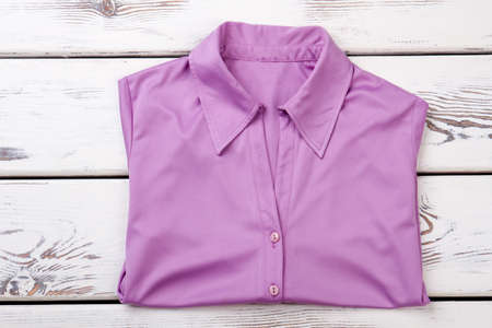 Female purple color buttoned shirt. Women formal blouse folded on white wooden background. Feminine business style apparel.の写真素材