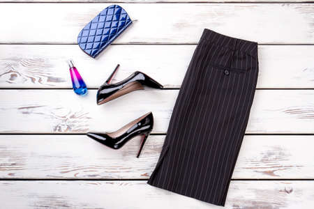 Women classic skirt, heels and accessories. Black leather high-heeled shoes, perfume and purse on wooden background. Female black pencil skirt and shoes.の写真素材