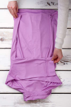 Caucasian women hands and purple shirt. Woman folding clothes on white wooden table. Store of feminine formal outfit.の写真素材