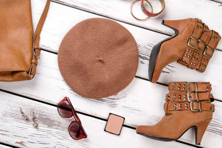 Stylized set of female fashion outfit. Stylish women brown boots and accessories on white wooden...