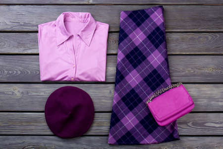 Set of female elegant attire. Women purple color shirt and skirt, wooden background. Feminine fashion clutch and beret. Ladies classy apparel flat lay.の写真素材