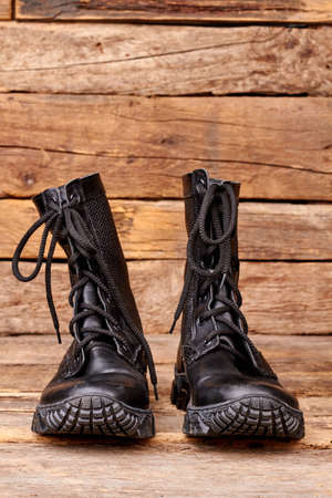 Pair black combat army boots. Wooden desk brown background.の写真素材