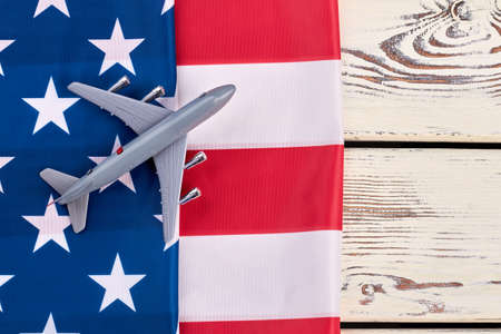 Flag of USA and toy air plane. Plastic toy jet plane and american flag on white wooden background. Flight to America concept.の写真素材