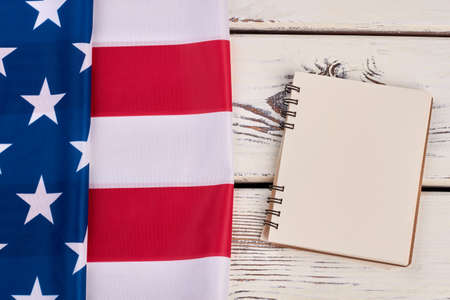 Flag of America and blank paper notebook. American flag and opened spiral binder notebook with copy space, white wooden background.の写真素材