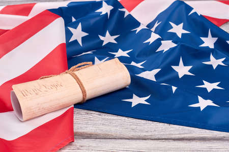 USA flag and ancient manuscript. Rolled-up constitution document on national flag of America, wooden background.の写真素材