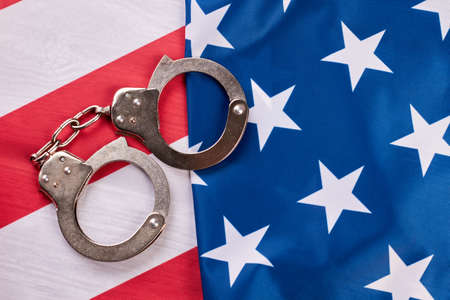 Handcuffs and American flag. Pair of metal handcuffs lying on USA national flag. Law and criminal.の写真素材