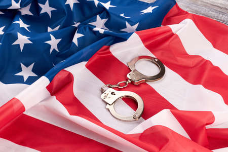 Flag of America and handcuffs. USA flag and pair of metallic handcuffs. Keep within the laws of the country.の写真素材