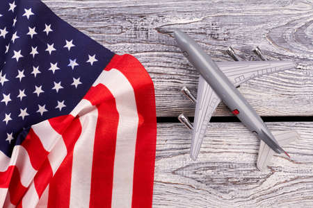 Plastic toy jet plane and flag of USA. American flag and grey toy air plane on wood close up. Flight to USA.の写真素材
