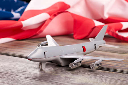 Grey toy air plane on wooden background. Plastic toy jet plane on table with blurred USA flag in the background. Flight to USA.の写真素材