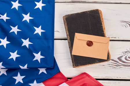 USA flag, old book and envelope. United States flag, ancient book and craft envelope on white wooden background, top view.の写真素材