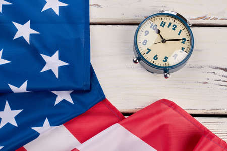 Close up USA flag and alarm clock. Mechanical alarm clock and flag of United States on light wooden background. Time to vote.の写真素材
