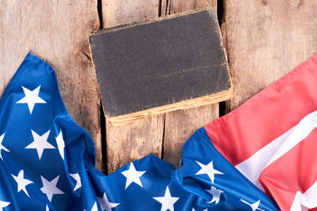 Closed vintage book and USA flag. United States satin flag and old hardcover book on rustic wooden boards.の写真素材
