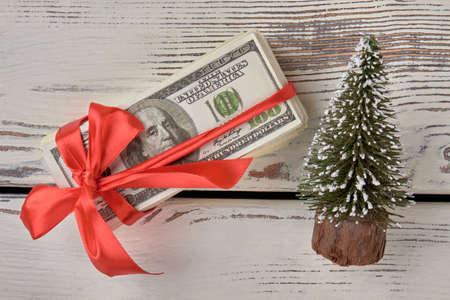 Christmas money gift concept. Dollars with red ribbon bow. White wood background. Top view, flat...