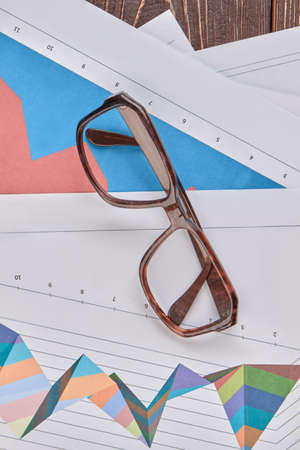 Glasses on financial papers with diagrams. Top view, close up.