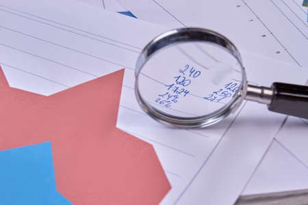 Analysing financial data with a magnifying glass. Diagram graphs and numbers with magnifier, close up.の写真素材