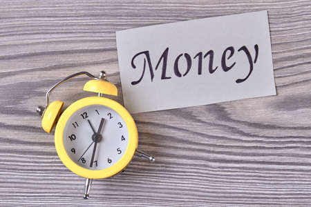 Time is money concept. Yellow alarm clock on wood.の写真素材
