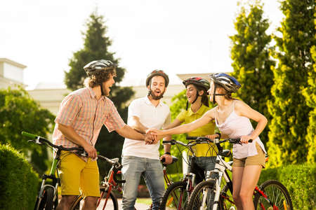 Cheerful students stacking hands together. Carefree group of friends having fun and smiling with bicycles during the summer day.の写真素材