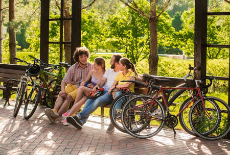 Group of friends resting in park. Young cyclists having rest sitting on bench in park. Students on summer vacation.の写真素材