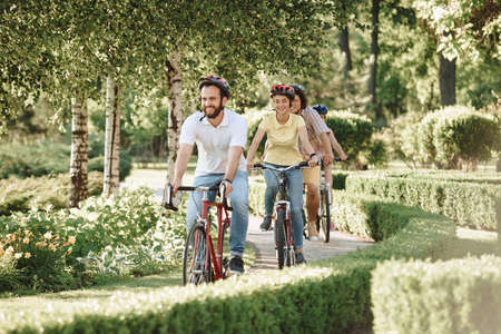 Cute sporty friends riding bikes in park. Group of friendly students spending time together outside. Summer vacation concept.の写真素材