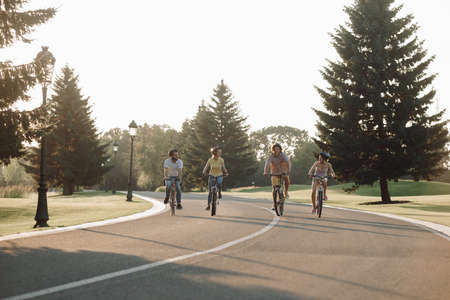 Group of smiling cyclists on the road. Group of happy young people in casual wear having fun while cycling together. Enjoying fun ride.の写真素材
