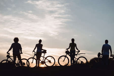Four young cyclists at beautiful sunset. Silhouettes of young people with bicycles at amazing sunset. Enjoying the nature.の写真素材