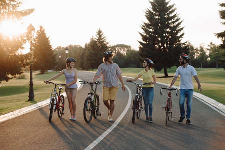 Group of cheerful cyclists walking with bicycles down the road. Four happy friends having fun with...